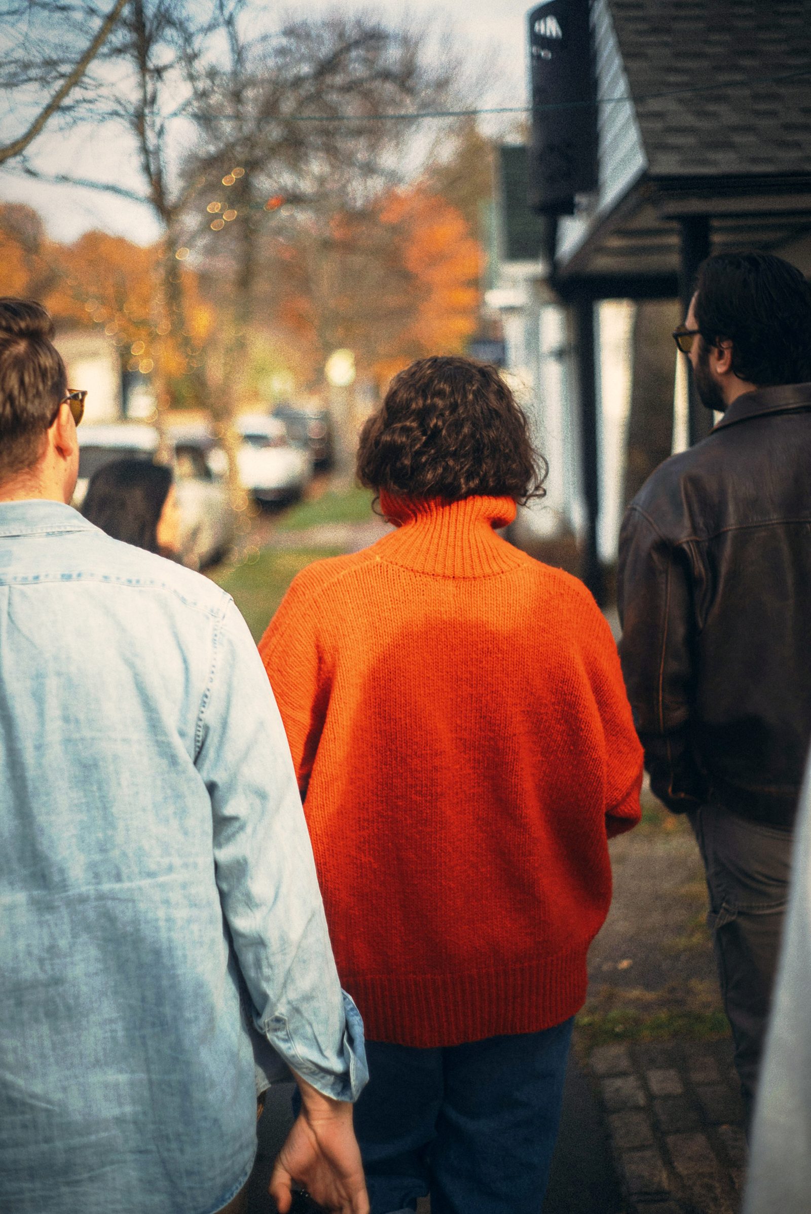 People walking a street past a lit shopfront in autumn.
