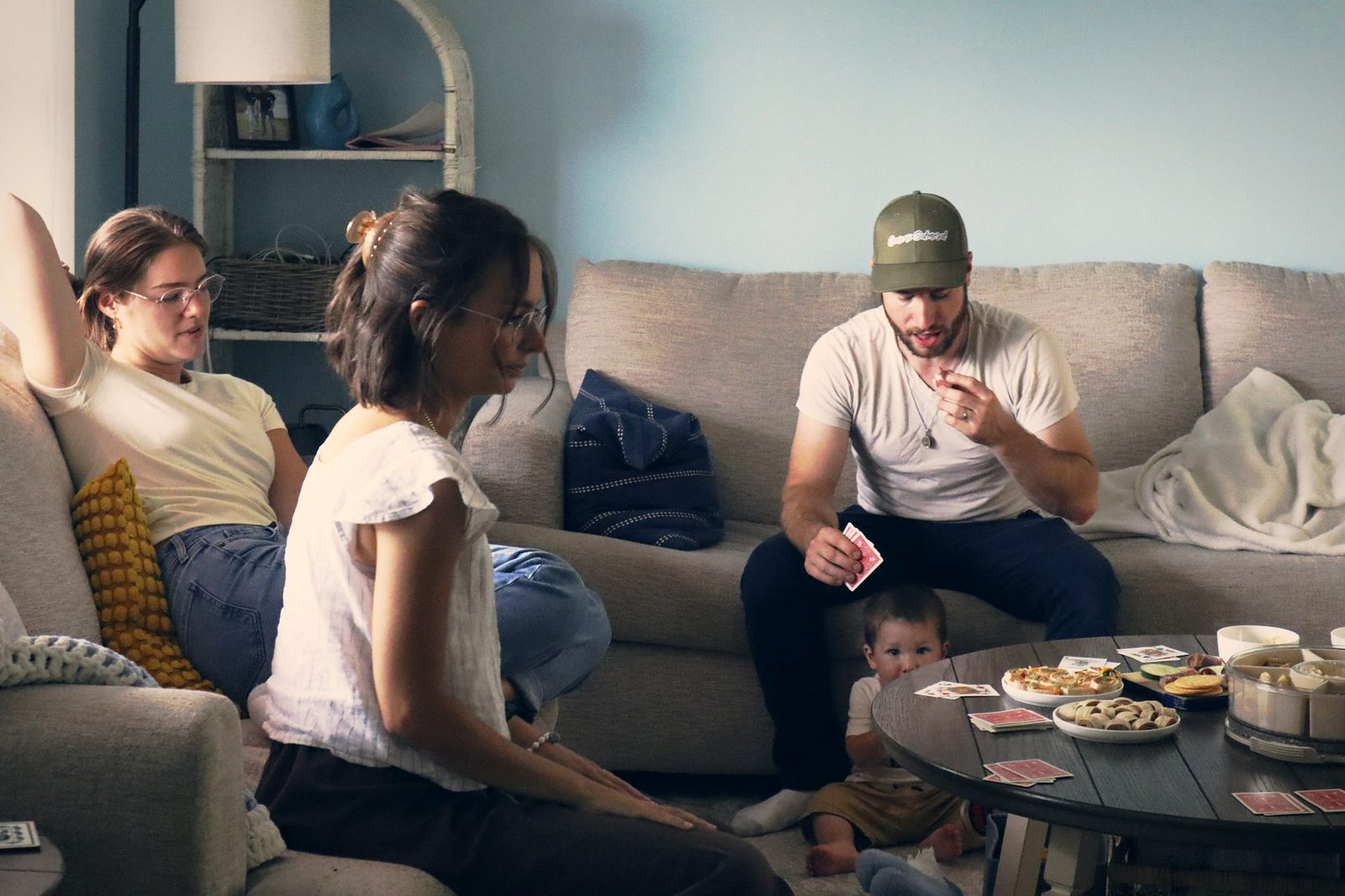 Friends playing cards around a coffee table in a living room, a toddler at their feet.