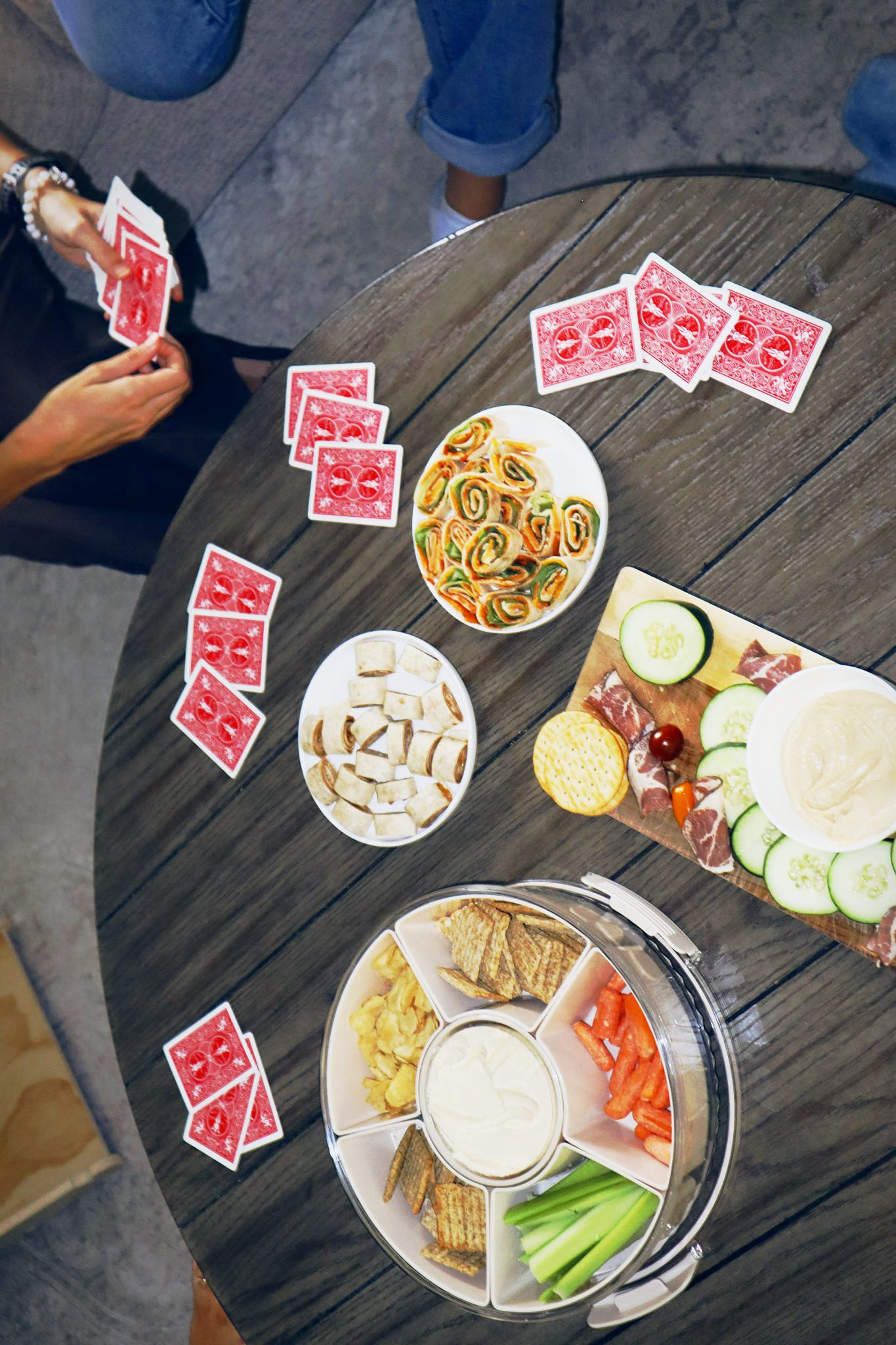A table seen from above with playing cards, pinwheels, crackers and a charcuterie board.